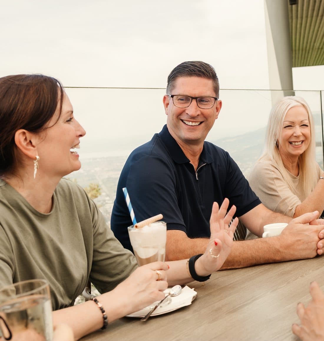 Kolleginnen und Kollegen lachen gemeinsam am Tisch auf einer Terrasse